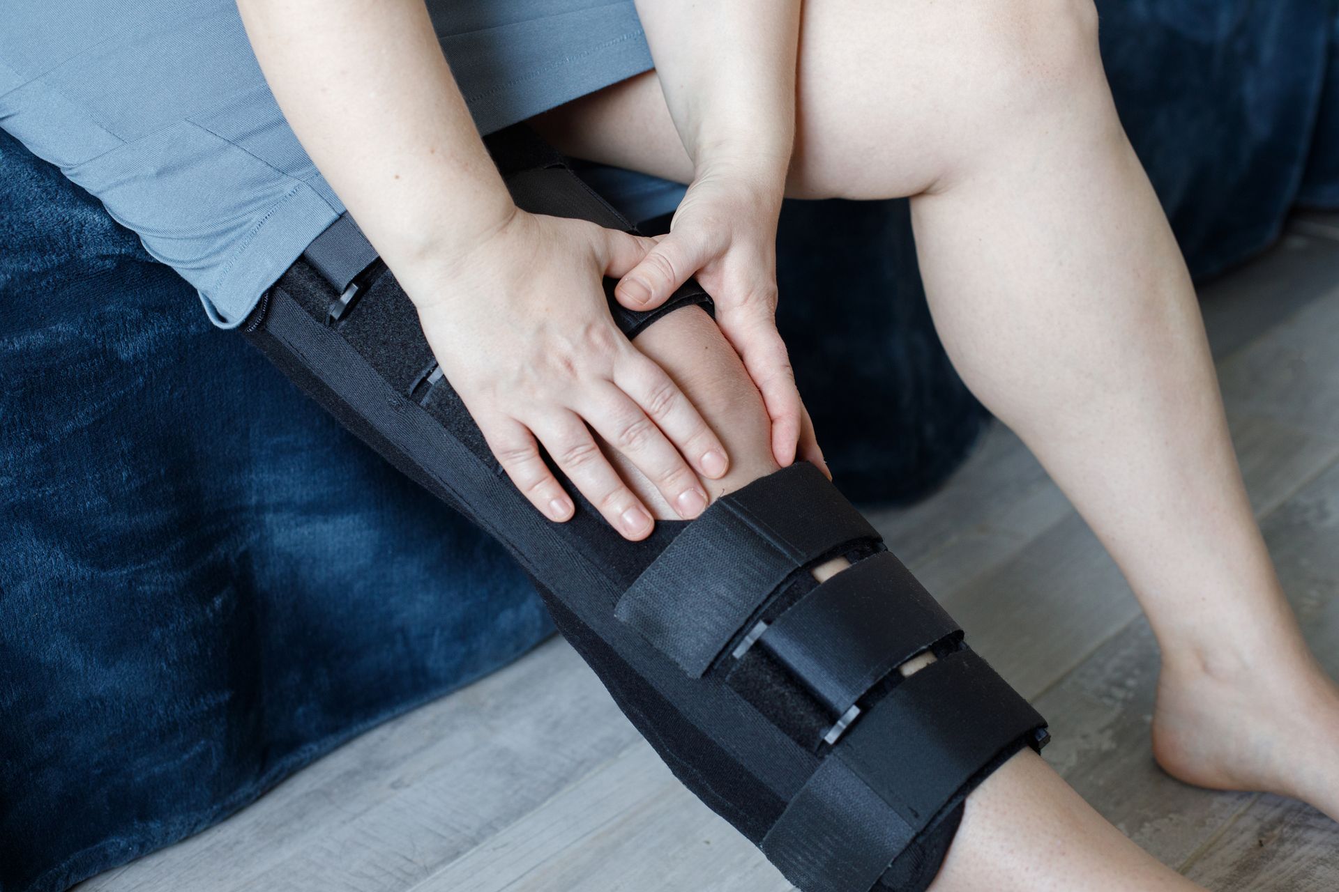 A person wearing a black knee brace on their leg, with hands resting on top of the brace.