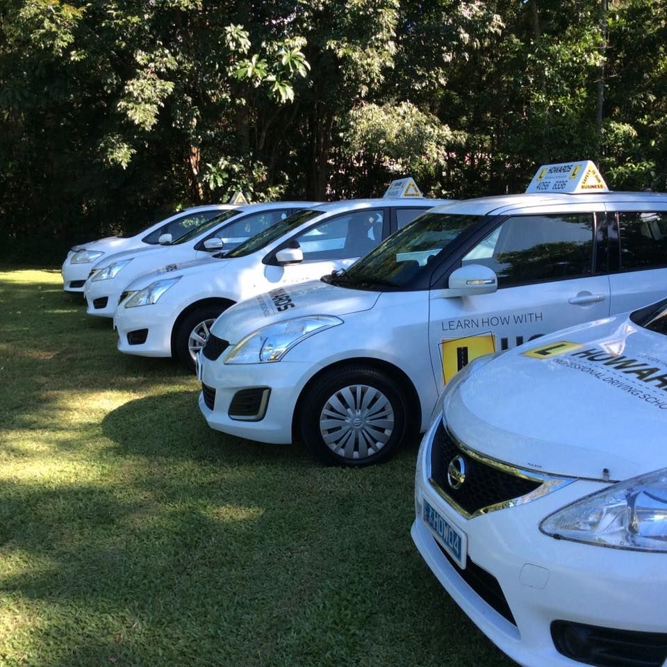 A Row of White Cars Are Parked in a Grassy Field — Howards Professional Driving School In Innisfail, QLD