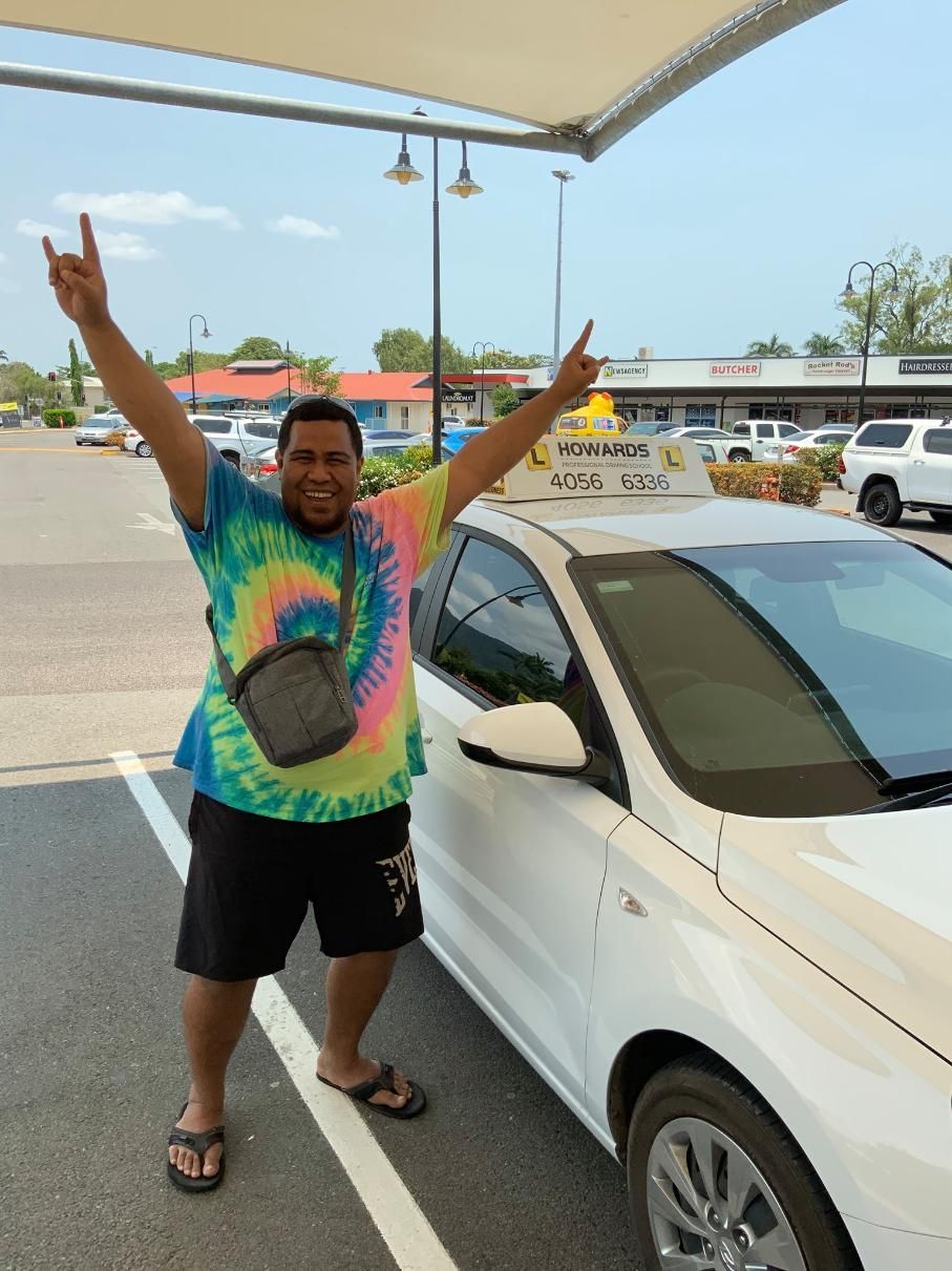 A Man in a Tie Dye Shirt is Standing Next to a White Car — Howards Professional Driving School In Cairns, QLD