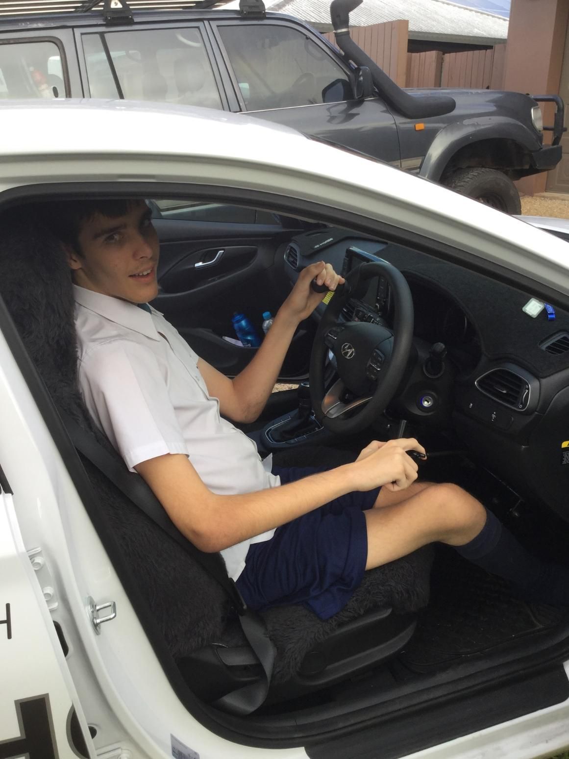 A Young Boy is Sitting in the Driver 's Seat of a White Car — Howards Professional Driving School In Cairns, QLD