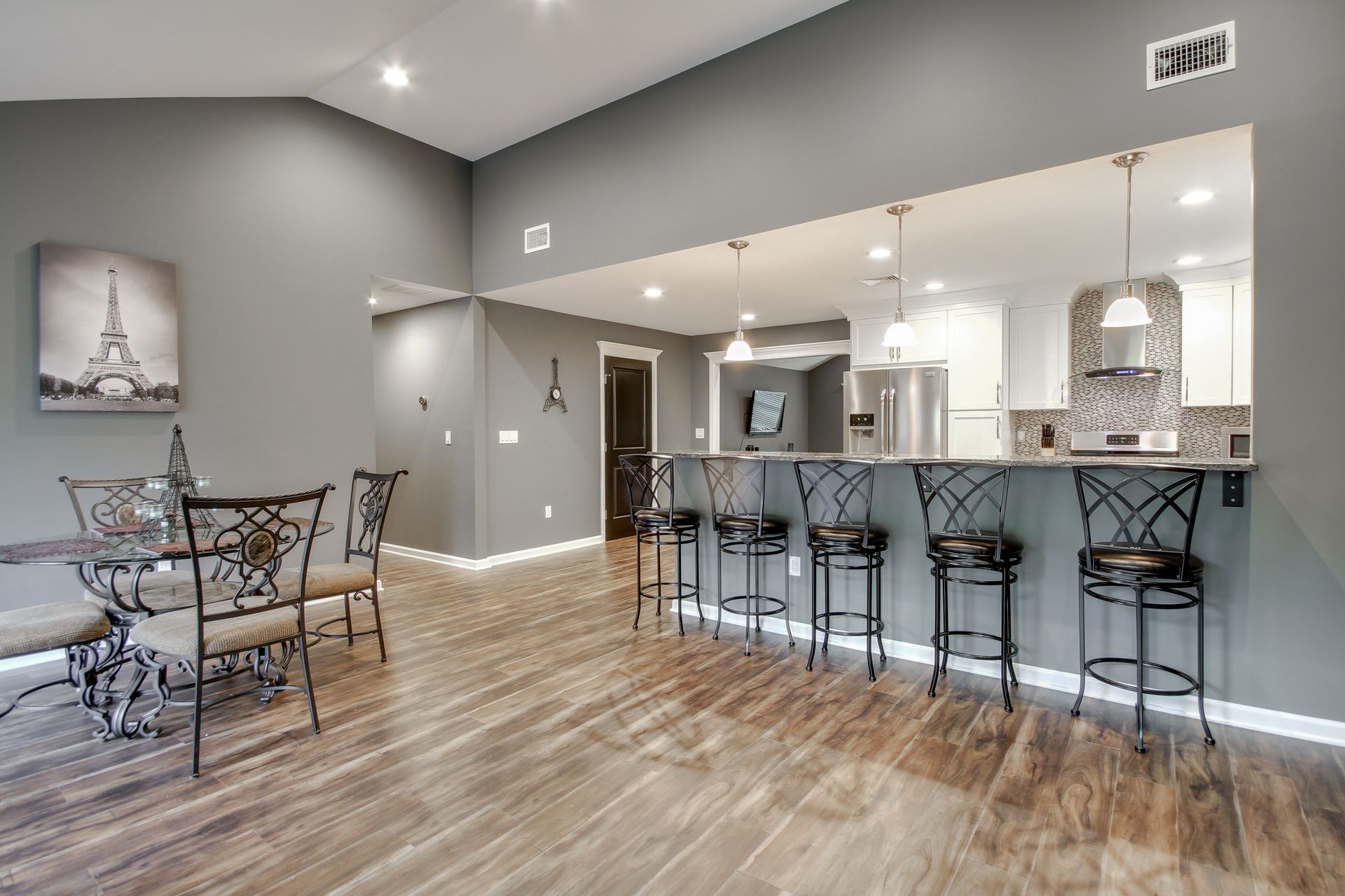 Dining area with bar seating, gray walls, hardwood floors, and view into the kitchen.