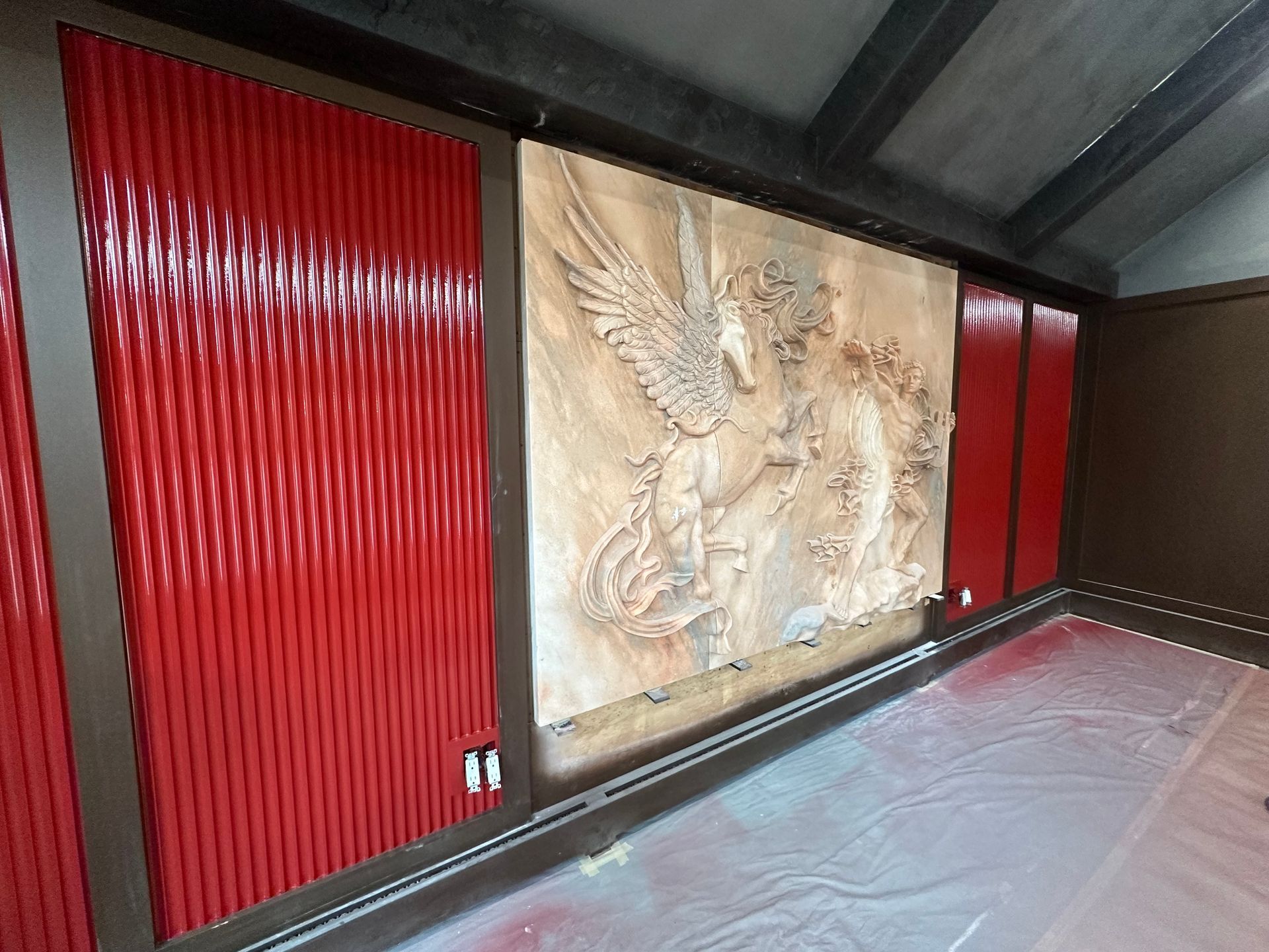 Red paneling frames a relief sculpture of figures with wings. Empty room with red and brown walls.