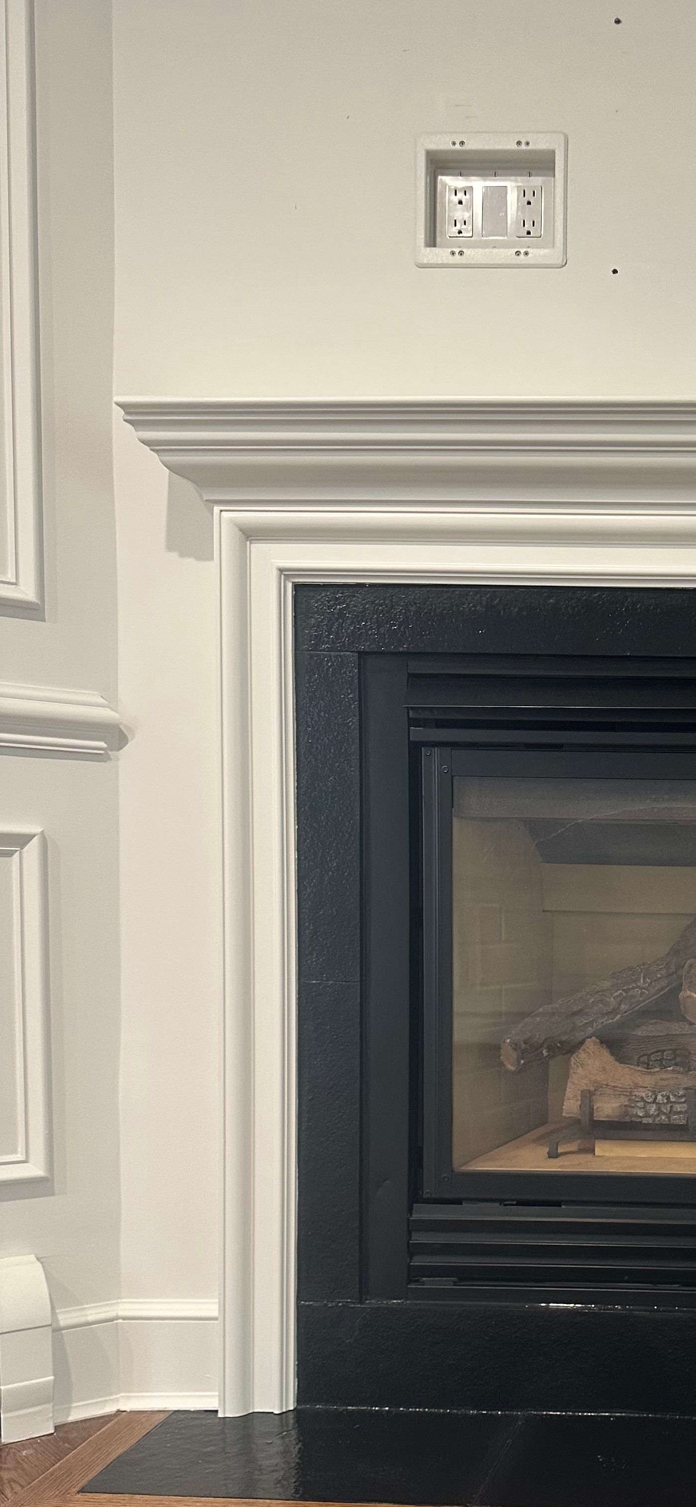 A fireplace with a black surround, white trim, and an electrical outlet.