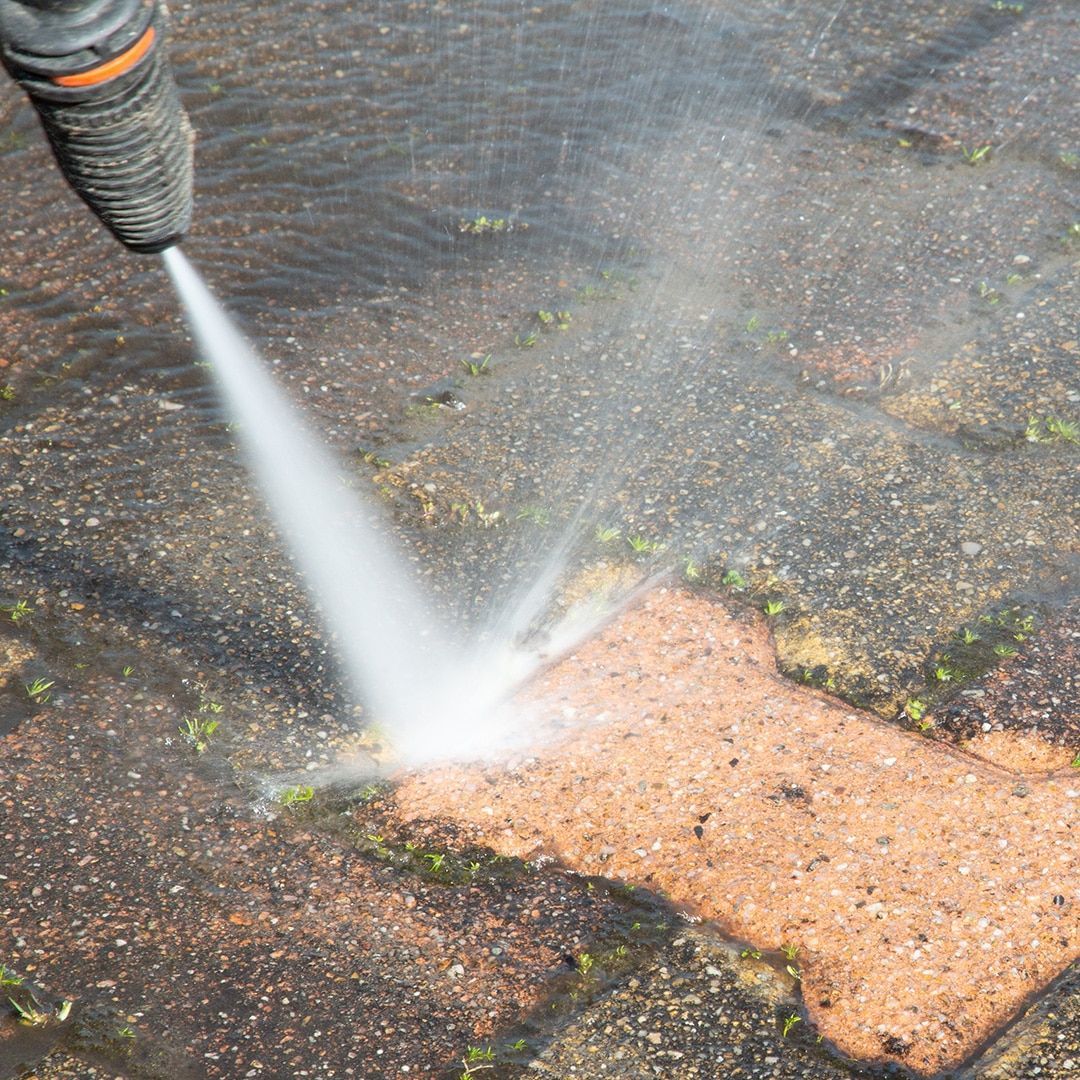 A pressure washer spraying water on a brick patio, removing dirt and grime.