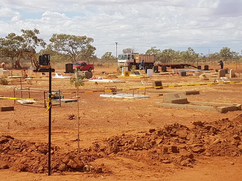 A cemetery with red dirt and graves. A truck and other equipment suggest construction or maintenance.