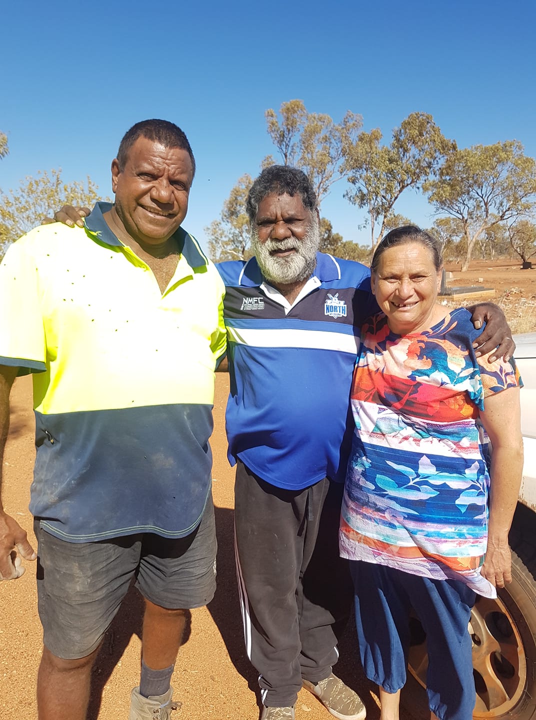 Three people stand outdoors, smiling.