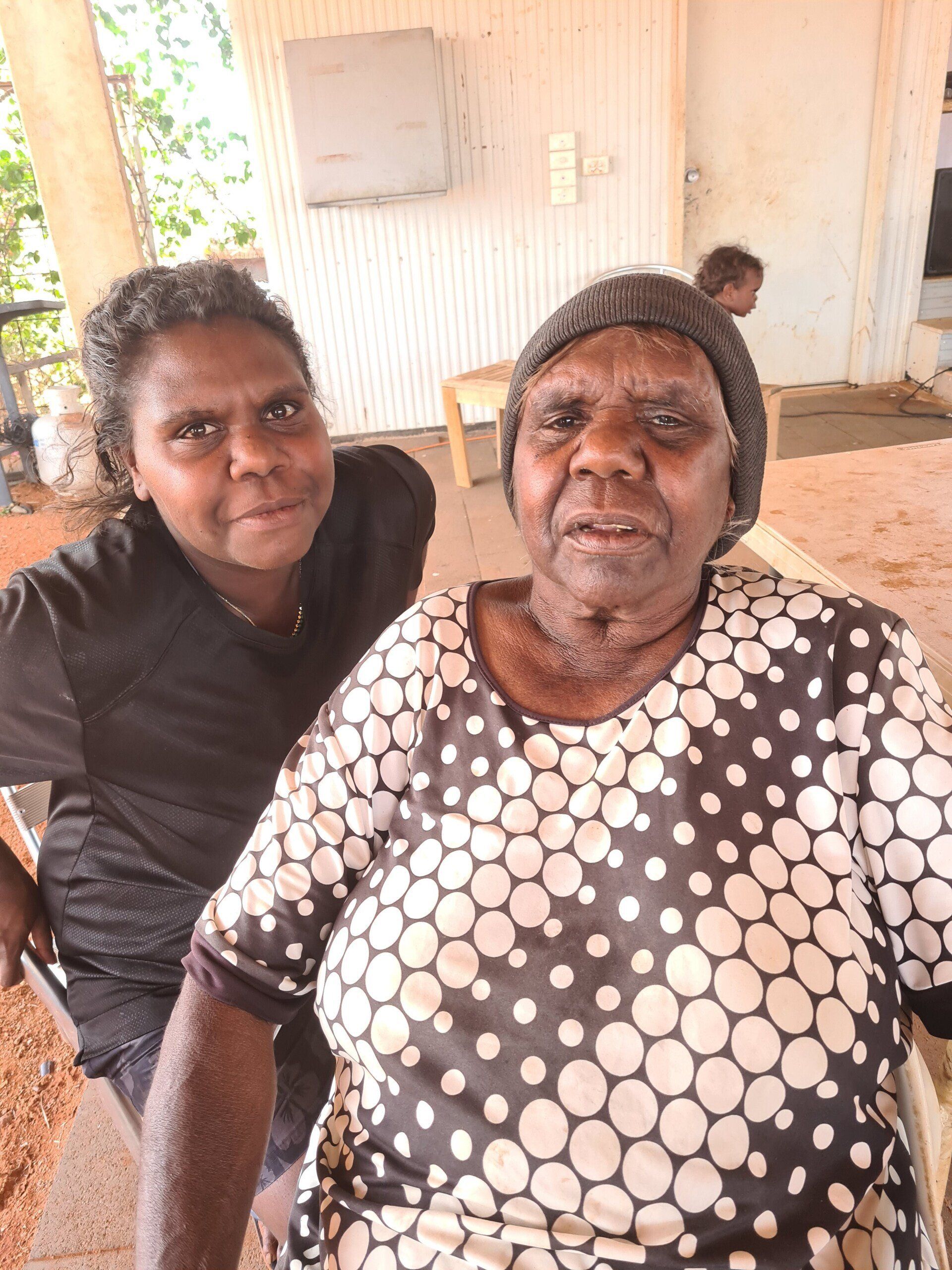 Two Indigenous Australian women pose for a photo outdoors.