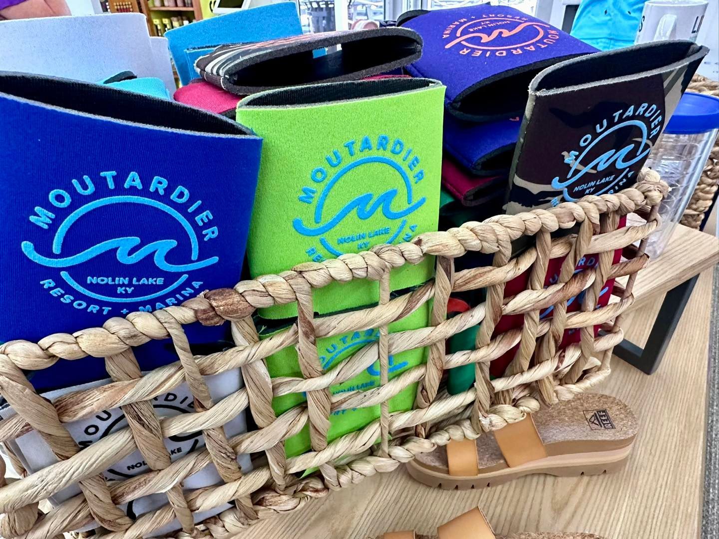A basket filled with can coolers and sandals on a table.