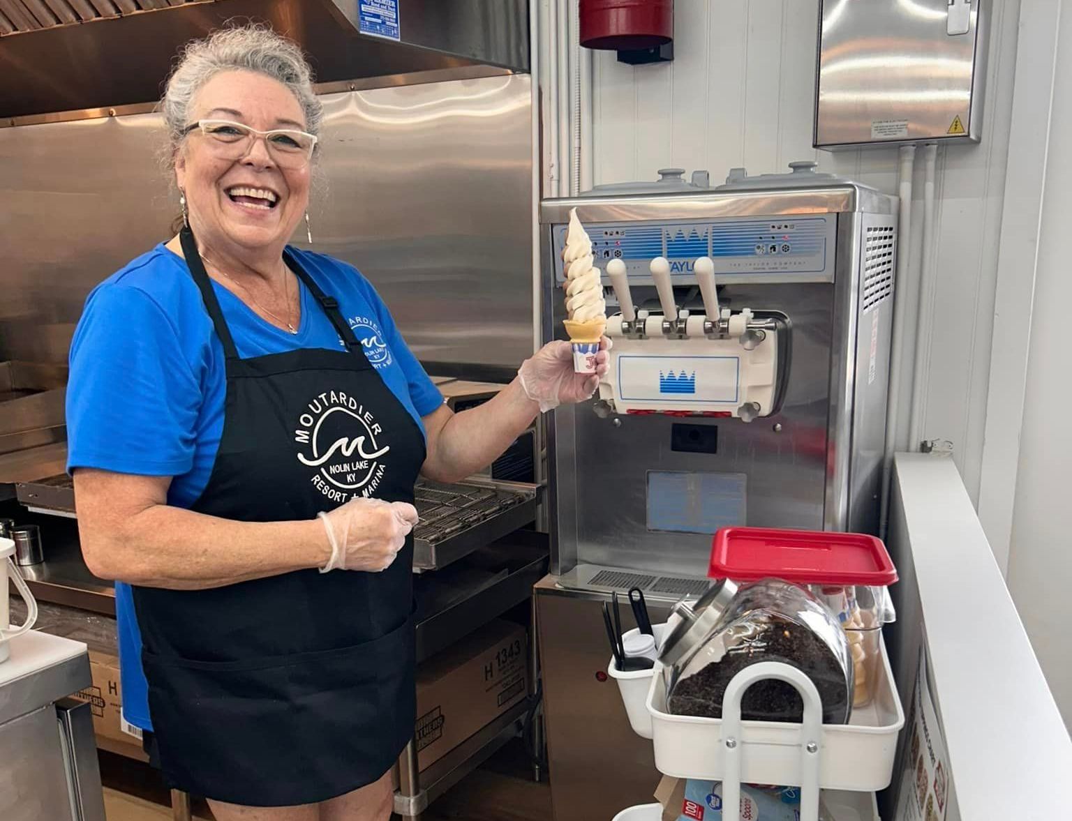 A woman is holding an ice cream cone in front of an ice cream machine.