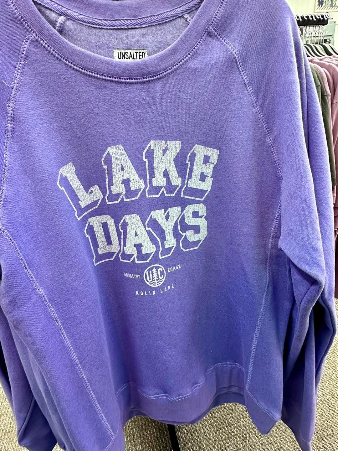 A purple sweatshirt with the words `` lake days '' on it is hanging on a rack.