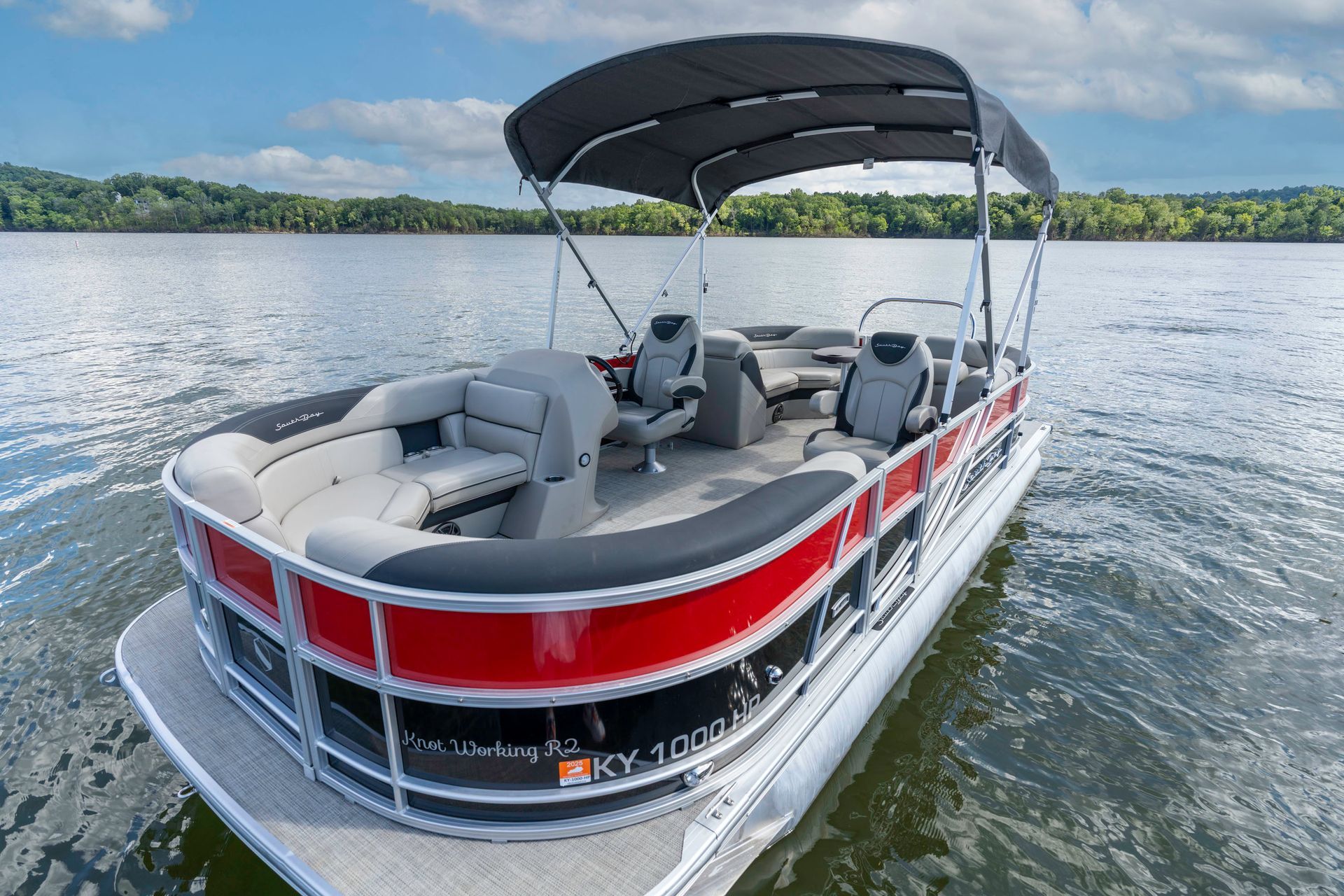 A red and black pontoon boat is parked on a trailer in a grassy field.