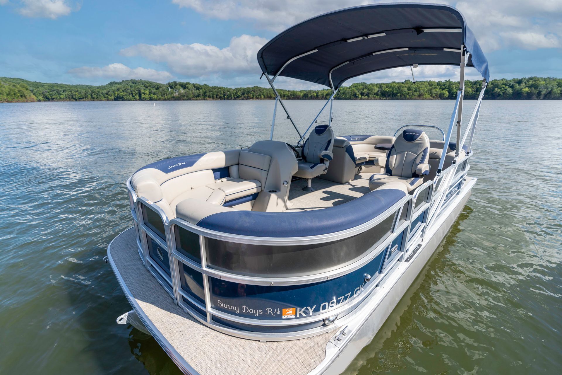 A pontoon boat is parked on a trailer in a grassy field.