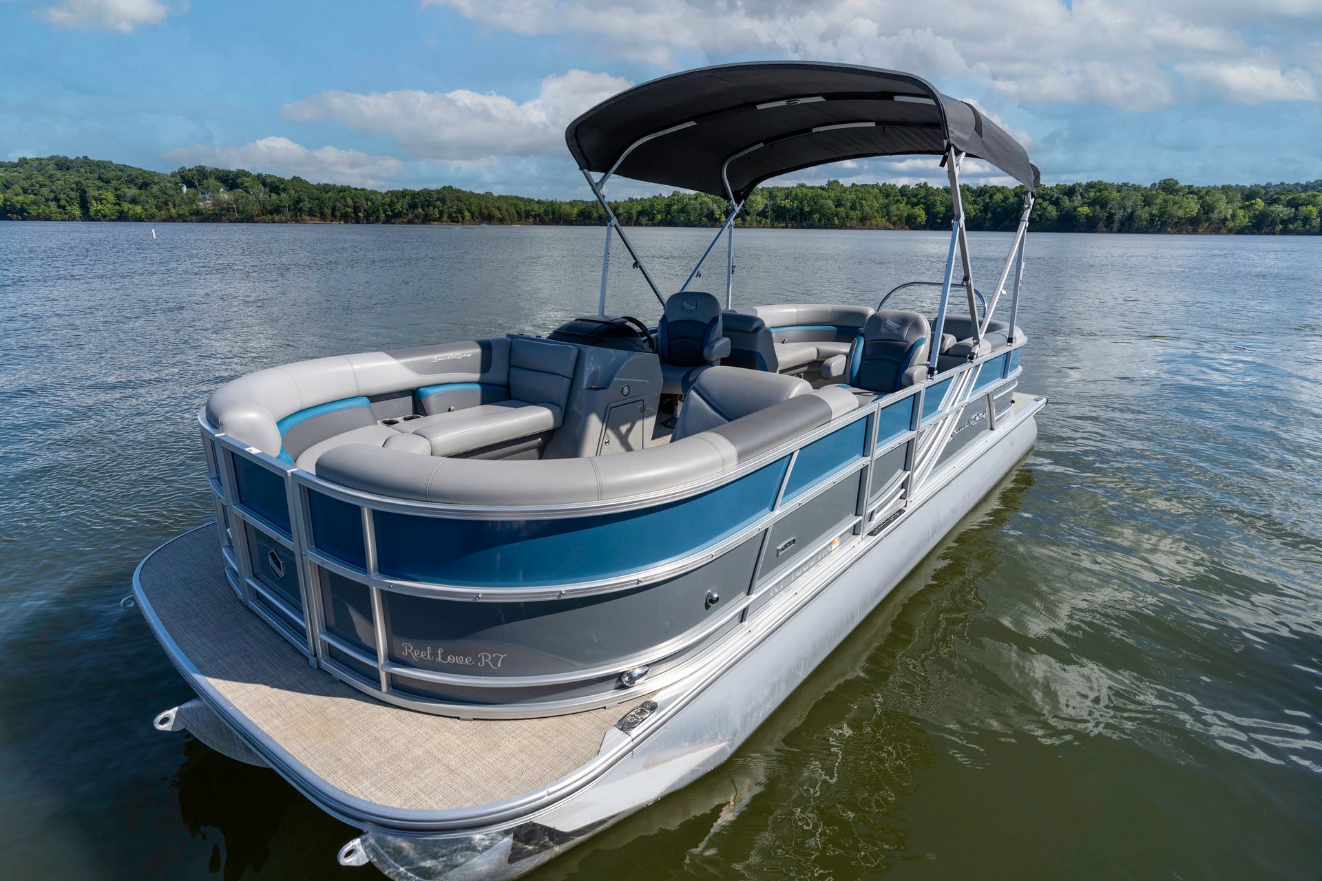 A pontoon boat is sitting on top of a trailer in a grassy field.