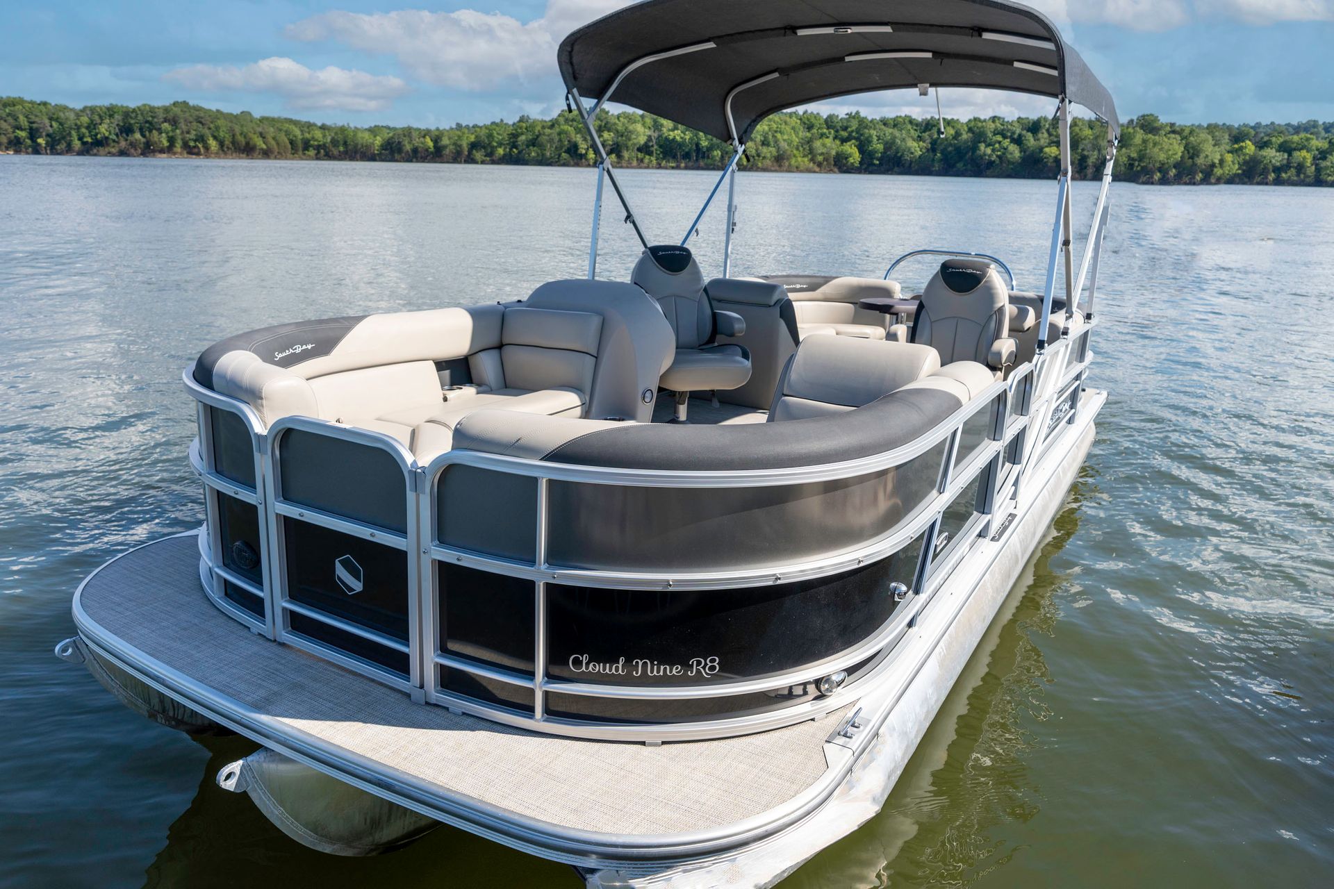 A pontoon boat is parked on a trailer in a grassy field.