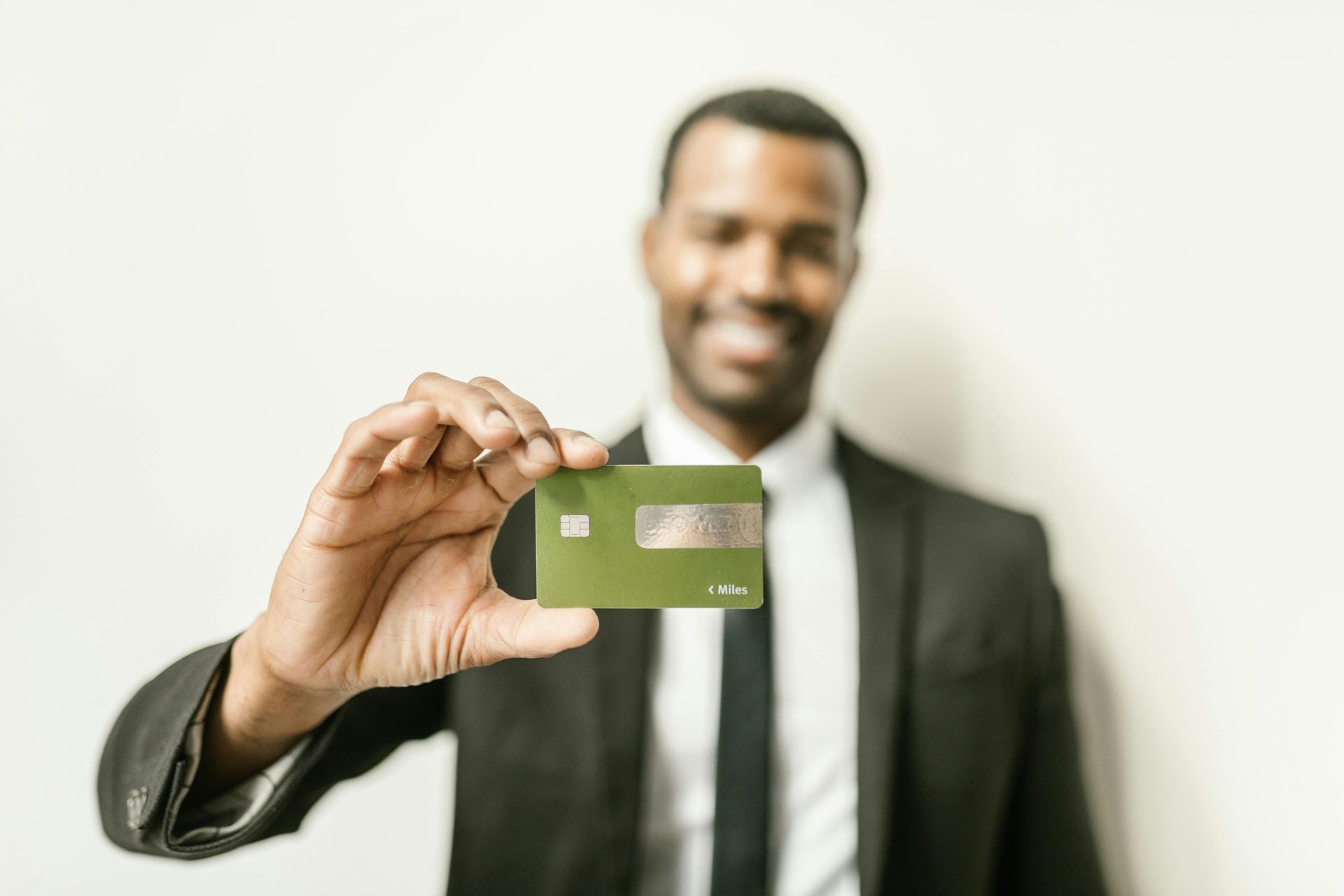 Man in suit smiles while holding up a green credit card against a white background.