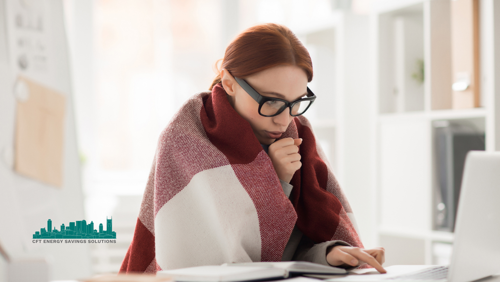 A woman wrapped in a scarf is sitting at a desk in front of a laptop computer.