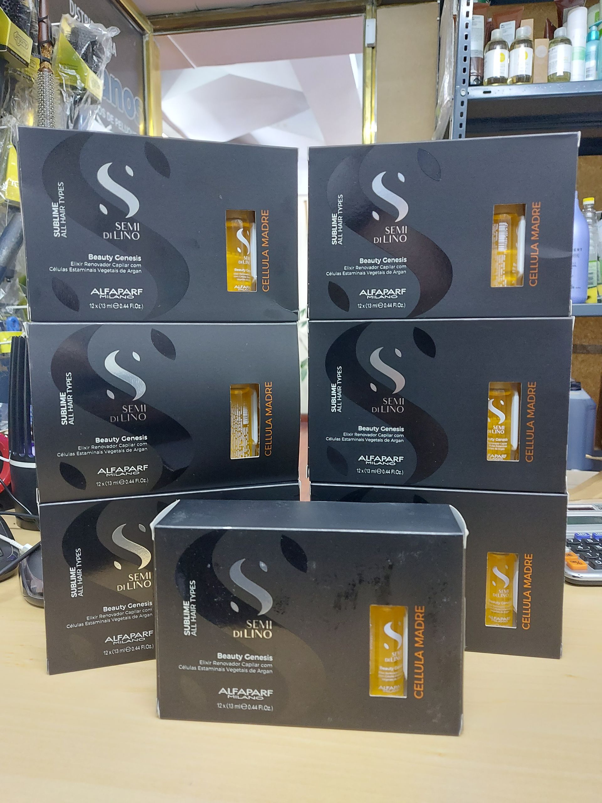 Cajas de productos para el cuidado de la piel, negras con detalles dorados, apiladas en una tienda, estantes y herramientas en el fondo.