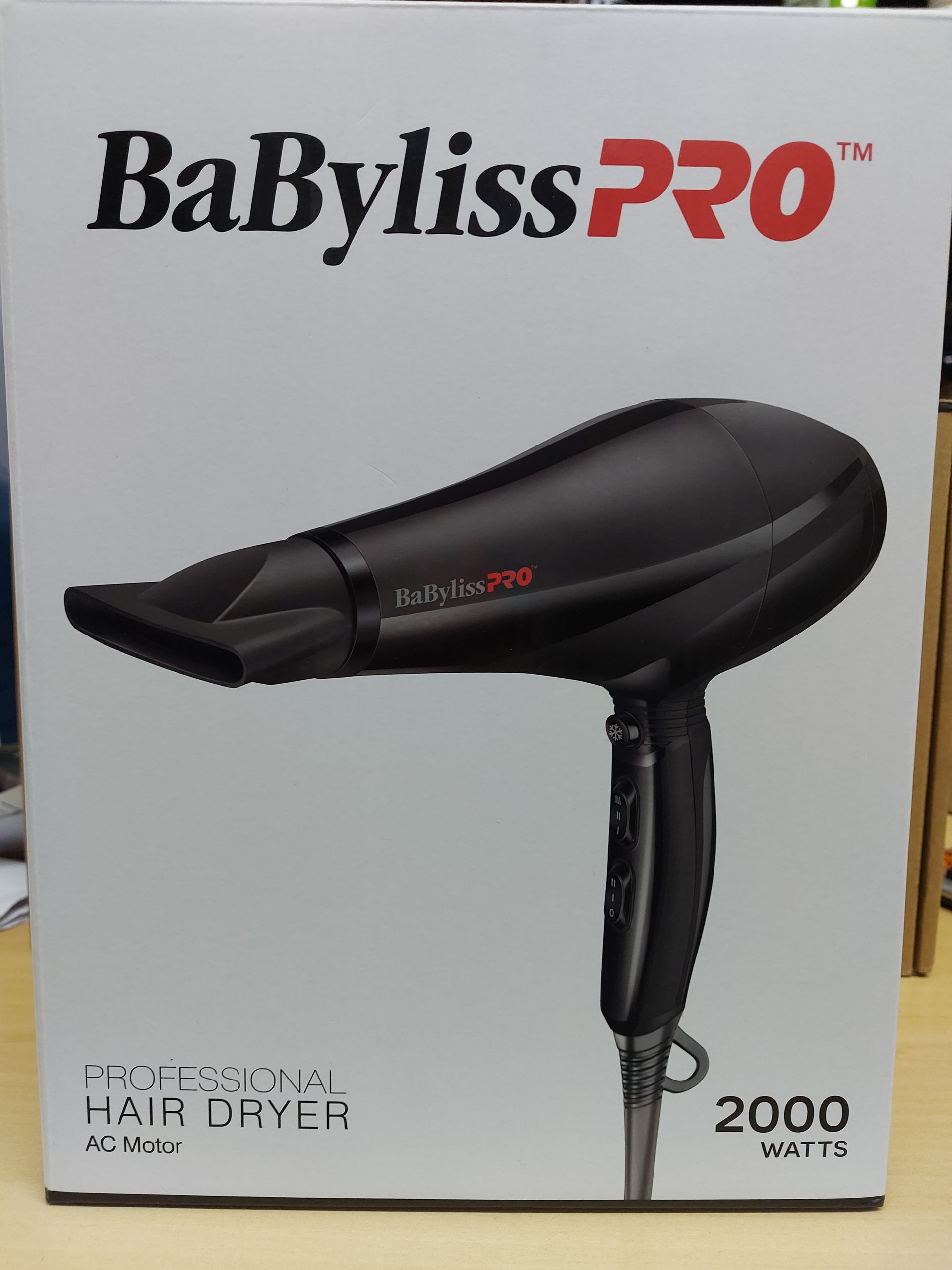Caja con un secador de pelo BaBylissPRO negro. La caja es blanca, con el nombre de la marca y una etiqueta que dice