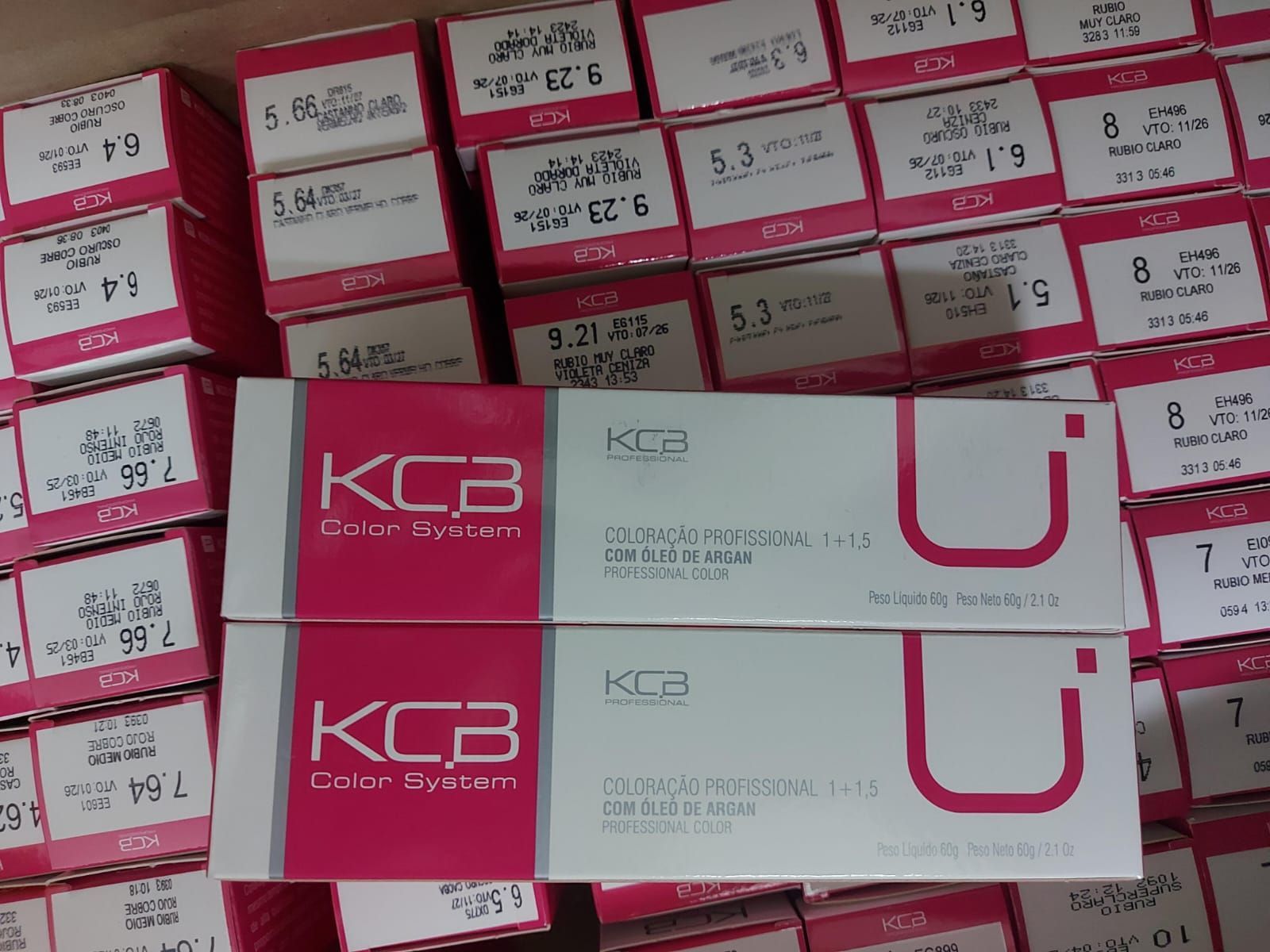 Cajas de tinte para el cabello del sistema de color KCB en varios tonos, apiladas con envases de color rosa y blanco.