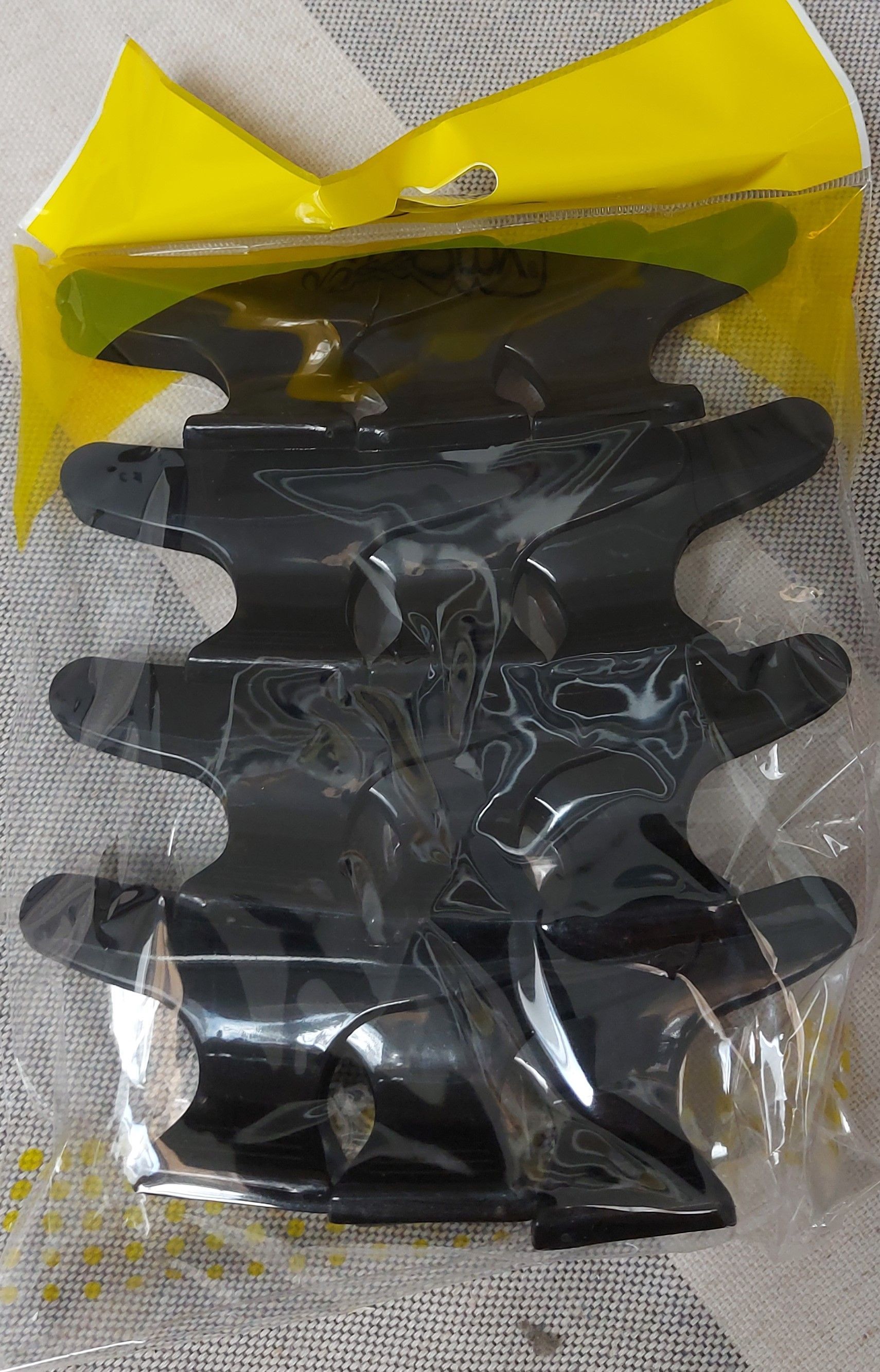 Pinzas para el cabello de plástico negro en un paquete de plástico transparente con un encabezado amarillo.