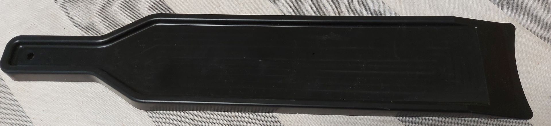 Pieza de moldura para tablero de instrumentos de automóvil de plástico negro, rectangular, con un extremo de manija estrecho y un pequeño orificio.