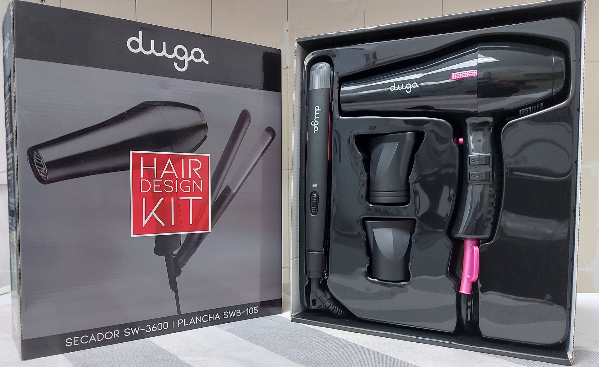 La caja del kit de diseño de cabello Duga se abre y revela un secador de pelo negro, una plancha y boquillas.