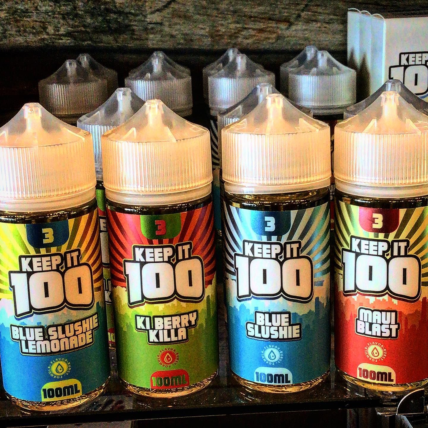 Several bottles of keep it 100 e liquid are lined up on a shelf