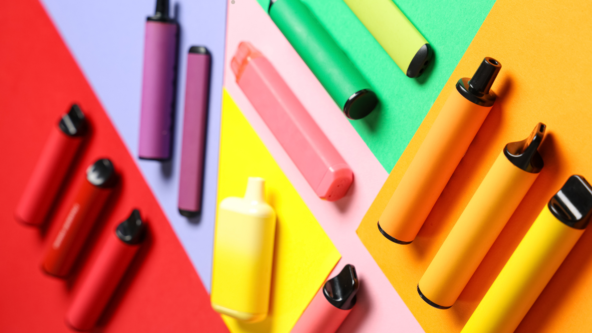 A collection of colorful disposable vapes arranged on vibrant, multi-colored backgrounds, featuring different shapes and colors, including red, yellow, green, and purple.