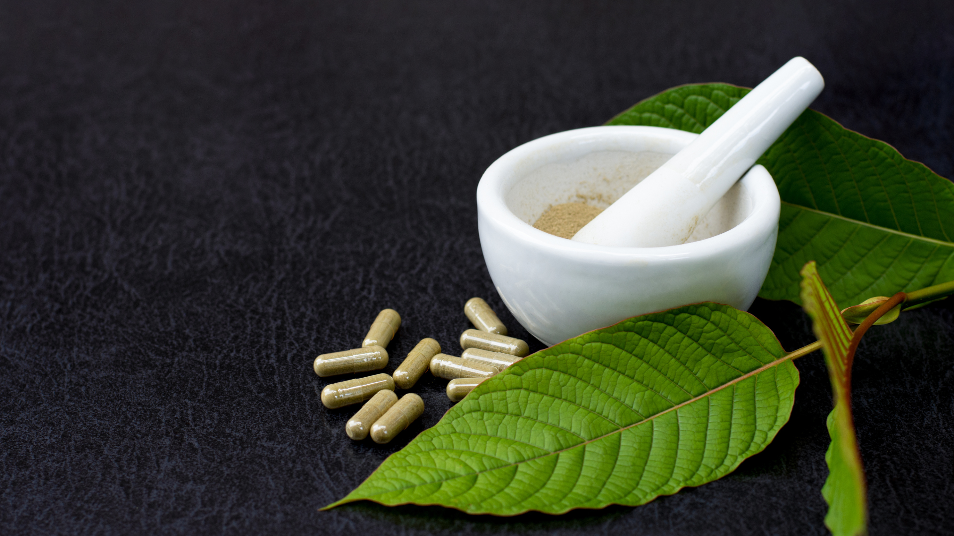 A mortar and pestle with pills and leaves on a table.