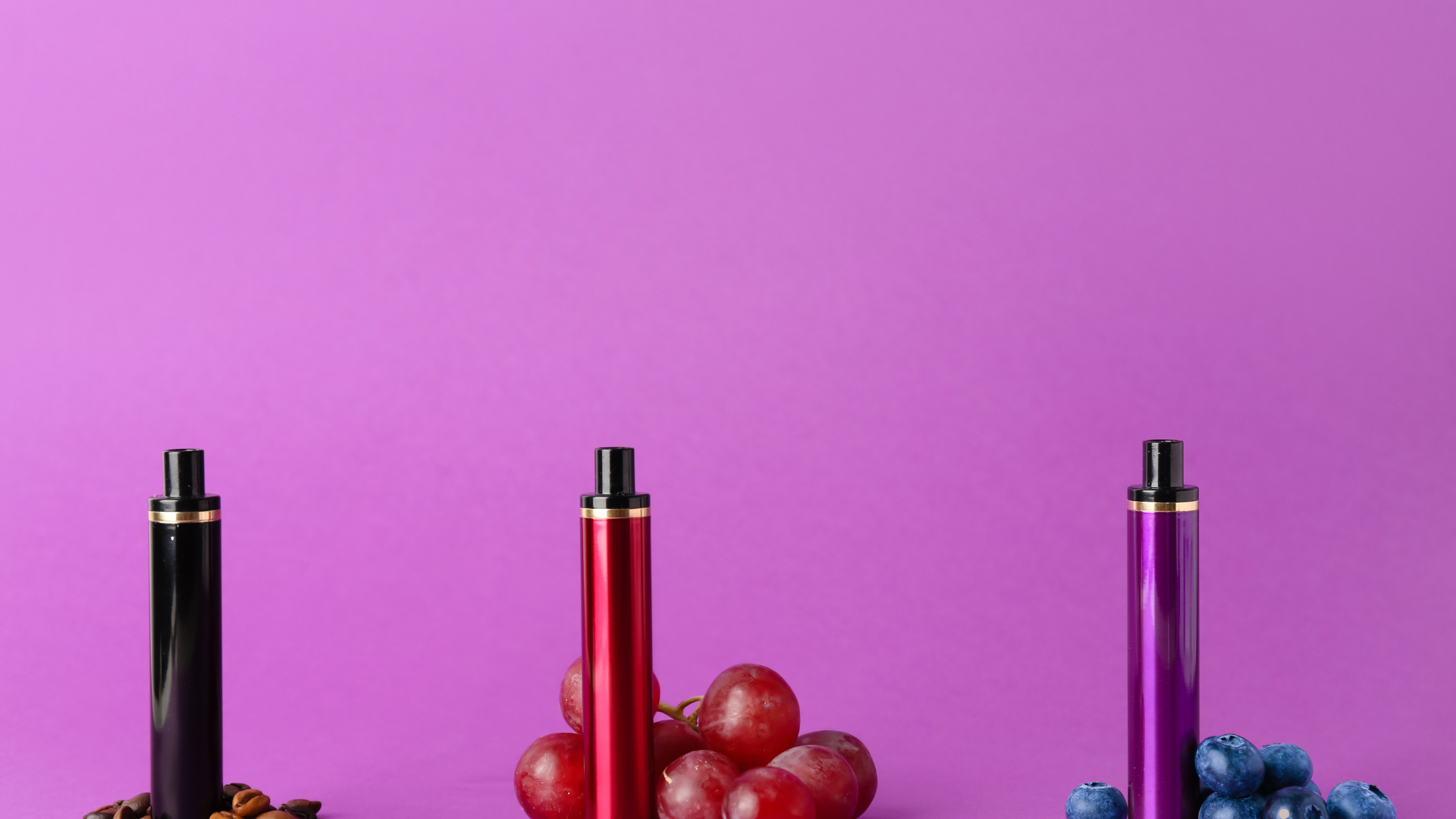 A colorful display of disposable vapes in black, red, and purple, surrounded by fresh grapes and blu