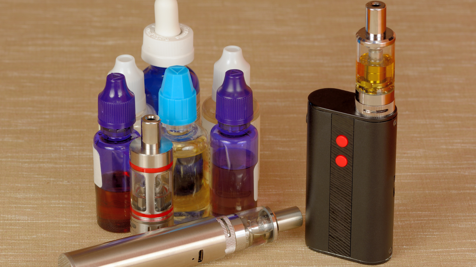 A collection of vape tanks and bottles of e-liquids in various colors, showcasing different flavors 
