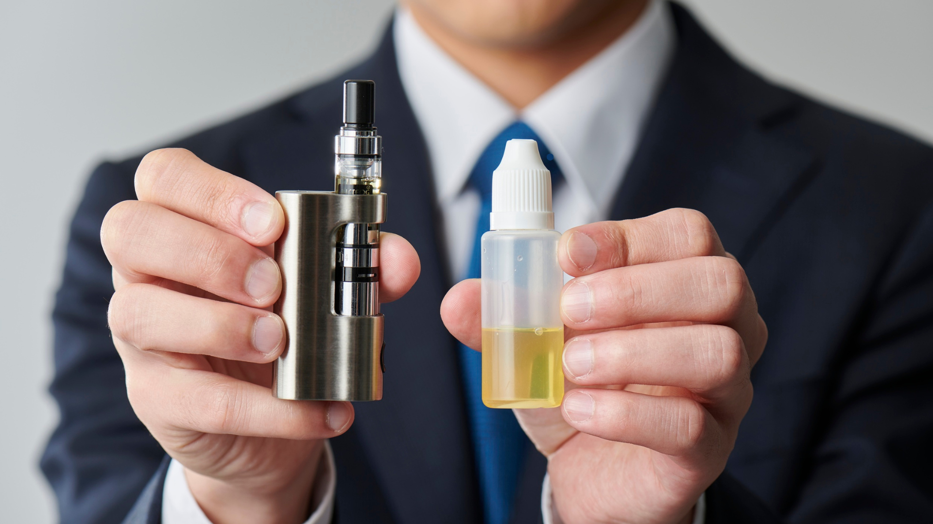 A person in a suit holding a vape device in one hand and a bottle of e-liquid in the other, demonstrating the process of refilling a vape.