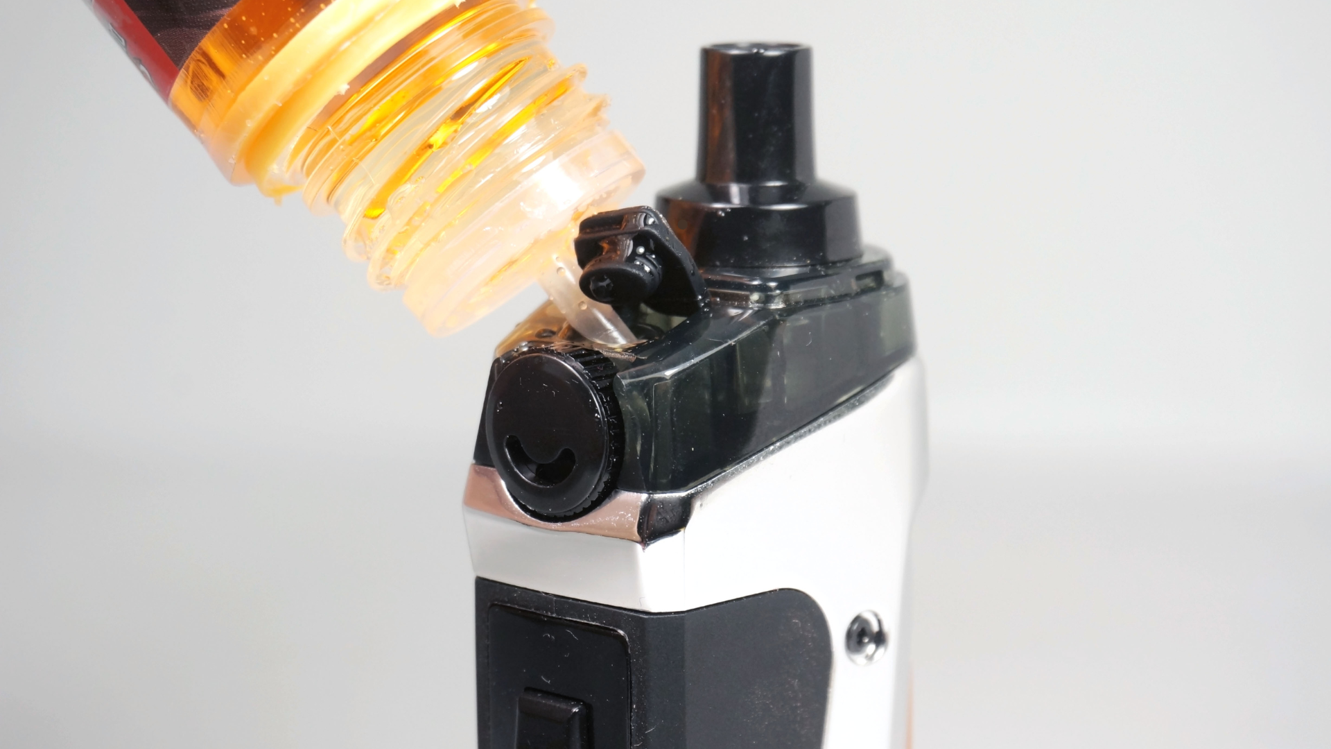 Close-up of a vaping device with a bottle of e-liquid being poured into its tank, illustrating the p