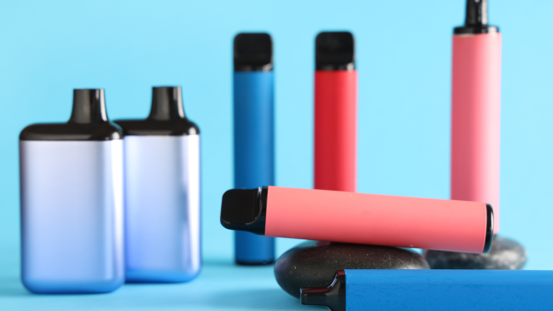 A variety of colorful disposable vapes arranged on a smooth surface with a blue background, showcase