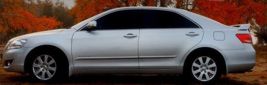 A white car is parked in a field with trees in the background.