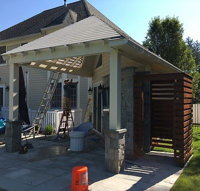 A man is standing on a ladder under a pergola in front of a house.