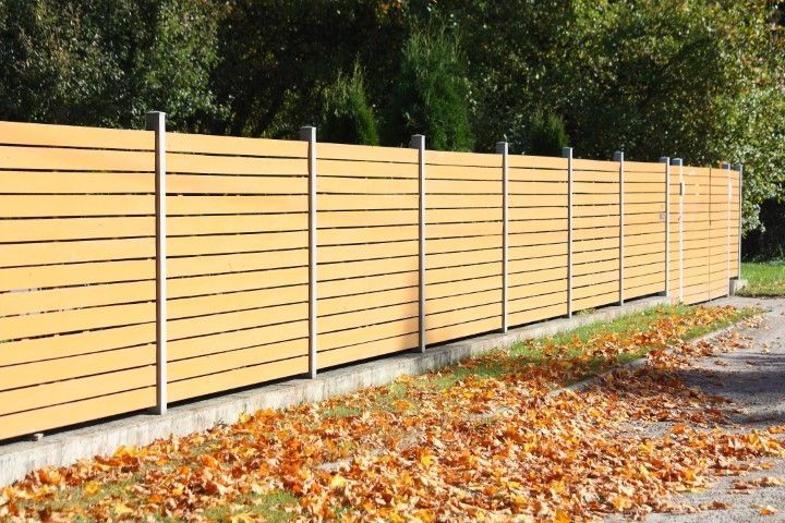 Wooden horizontal slat fence with silver posts; fallen leaves on the ground.