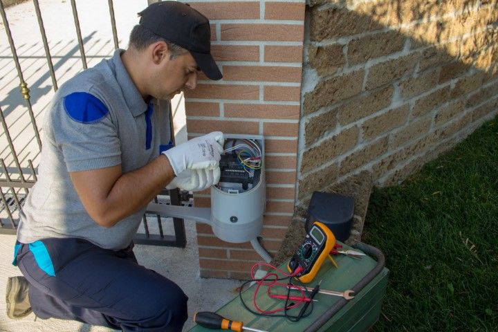 Man in uniform repairing electrical box with multimeter outside.