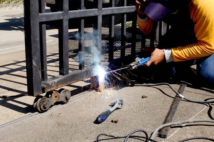 Person welding a black metal gate outdoors. Sparks fly from the torch.