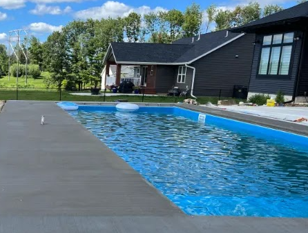 There is a large concrete swimming pool in the backyard of a house.