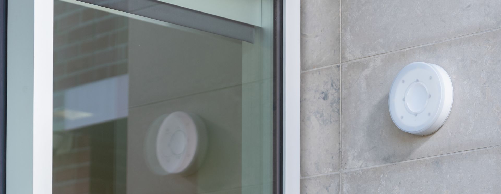 A white round object on a light grey wall and reflected on a window.