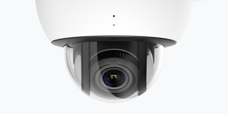 White security camera with a protective sun visor, outdoors.