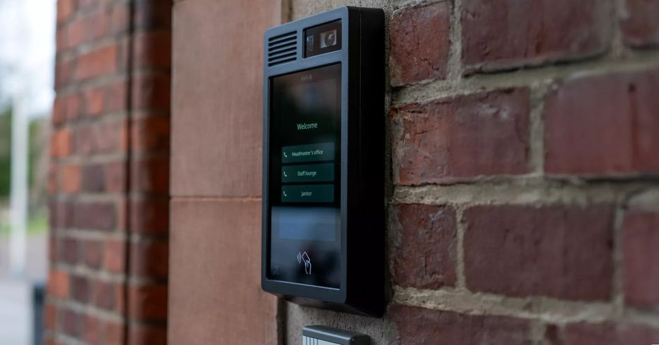 Black intercom panel mounted on a brick wall with a digital display and buttons.
