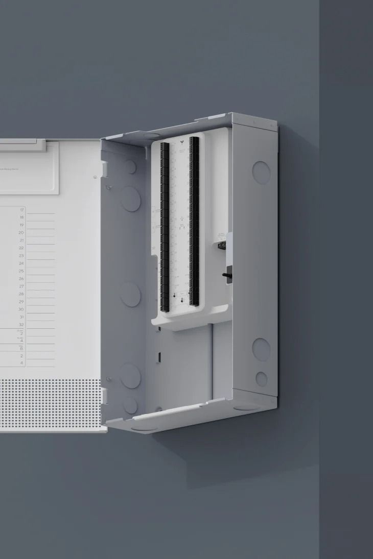 Gray electrical enclosure, open, mounted on a gray wall, showing interior components.