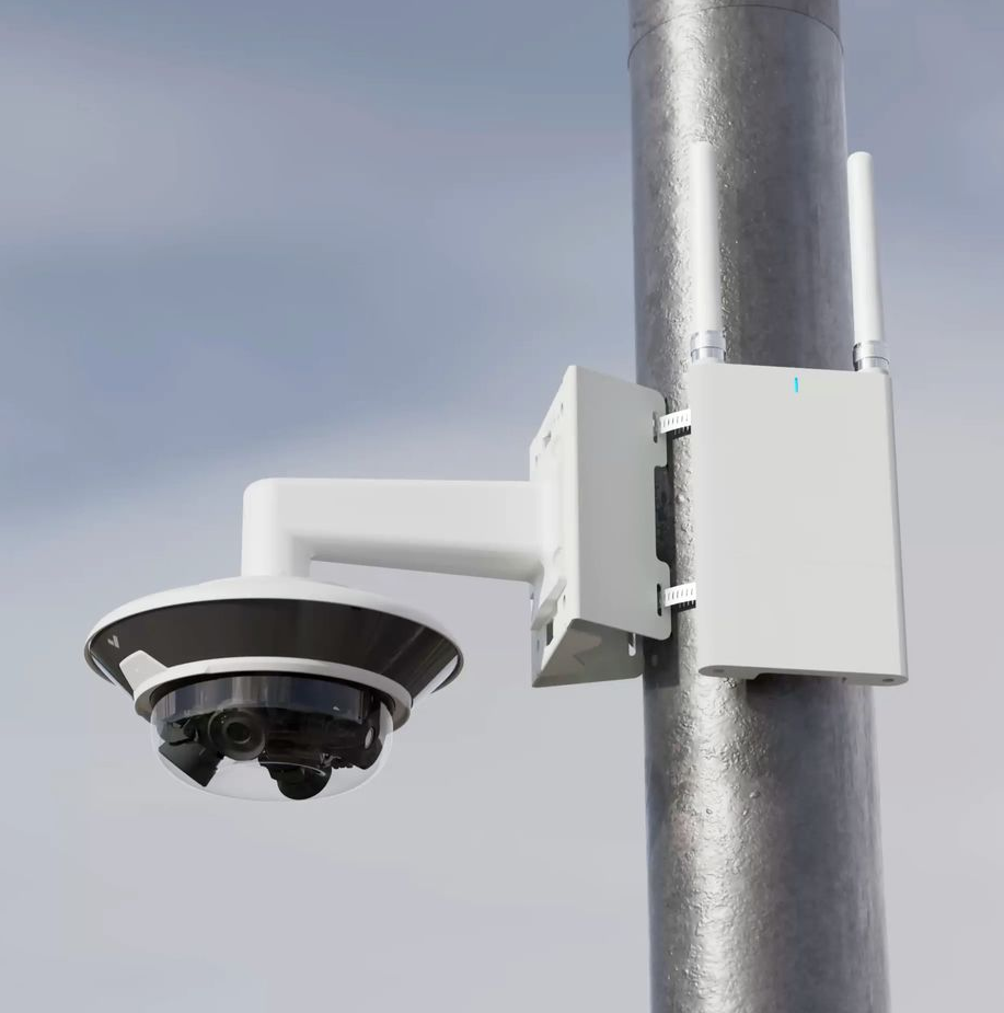 Security camera on a metal pole, with a dome camera and a white box with an antenna.