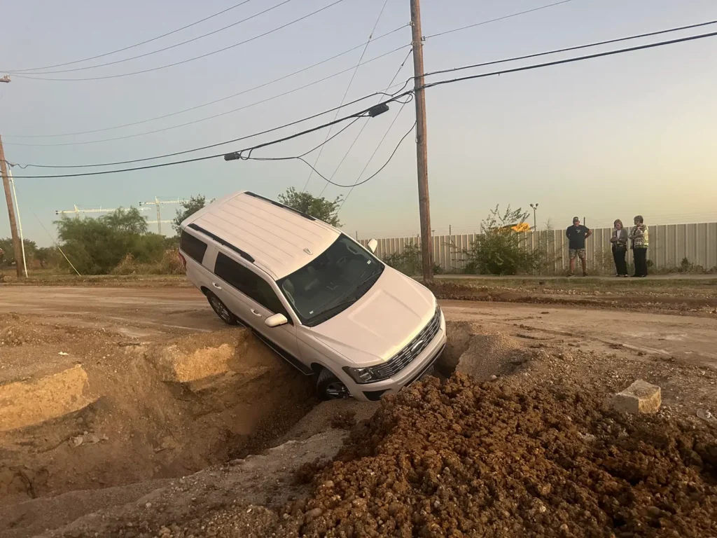 A white suv is stuck in a hole in the ground