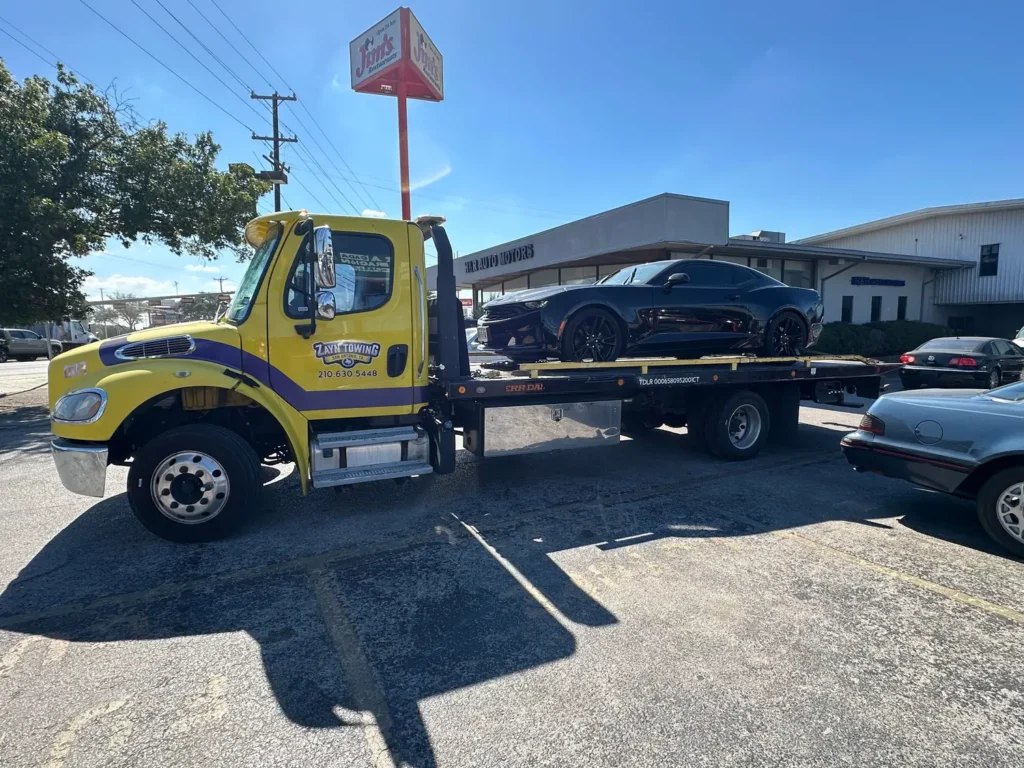 A yellow tow truck is towing a black car in a parking lot.