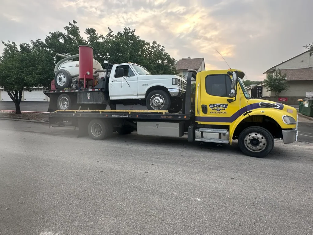 A yellow tow truck is carrying a white truck on its back.