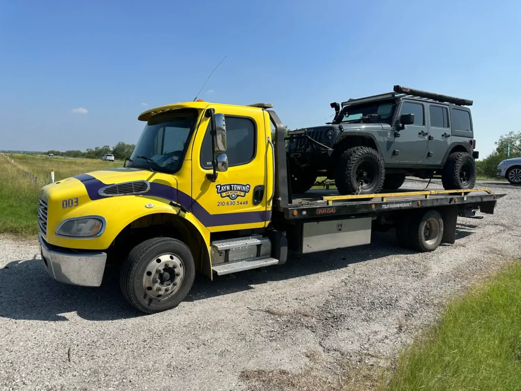 A yellow tow truck is carrying a jeep on the back of it.