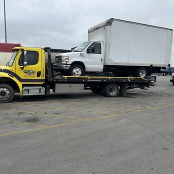 A yellow tow truck is towing a white truck in a parking lot.
